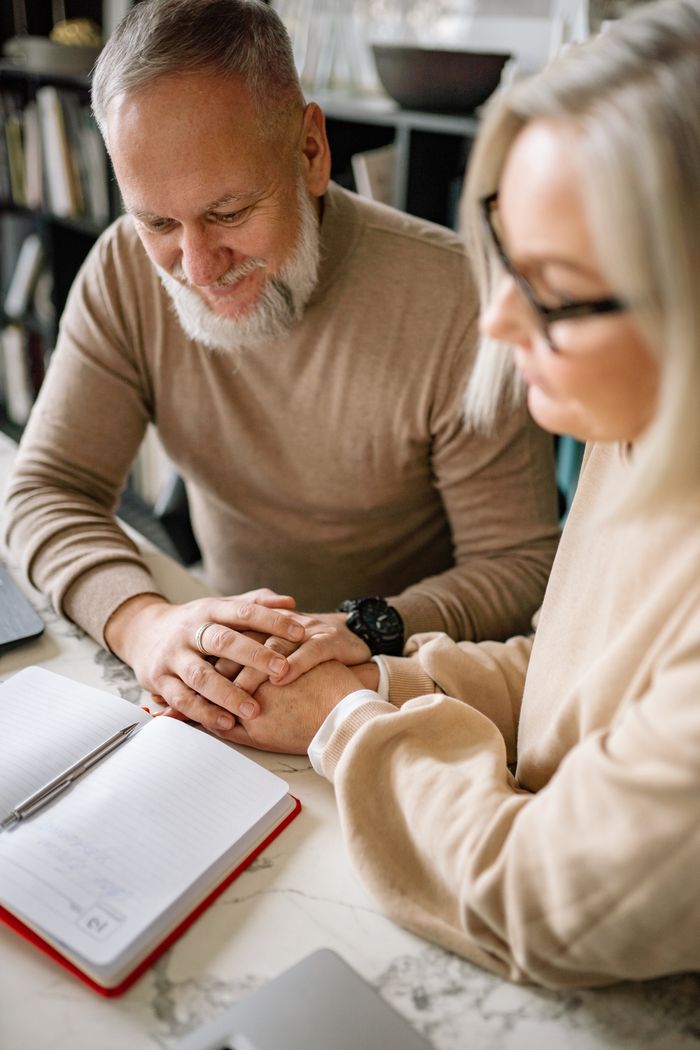 Senior couple holding hands and sharing a peaceful moment over a notebook at home.